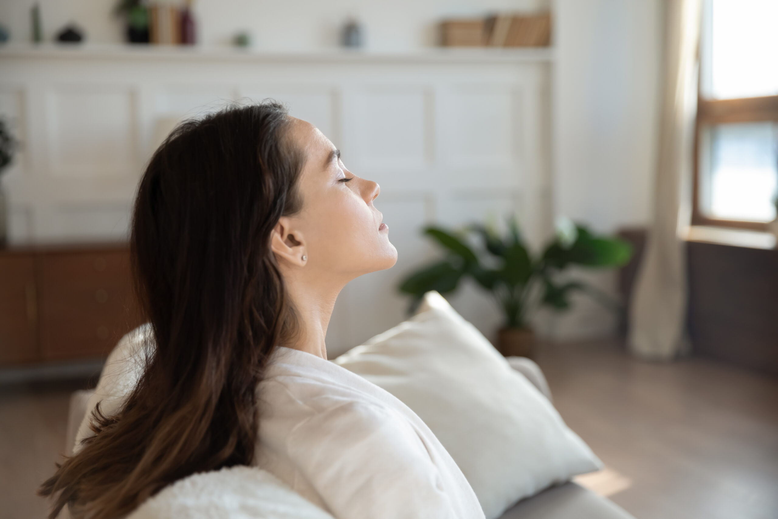 Serene lady taking pause meditating on sofa with closed eyes